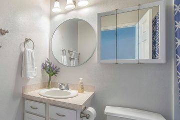Petite salle de bains minimaliste Pano avec toilettes blanches et miroir contre un mur uni. Un rideau de douche bleu imprimé donne une touche de couleur à l’intérieur des toilettes résidentielles.